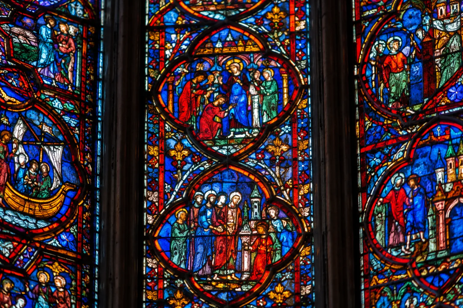 Détail de panneaux de vitraux médiévaux, où les lignes de plomb délimitent de petites scènes colorées.