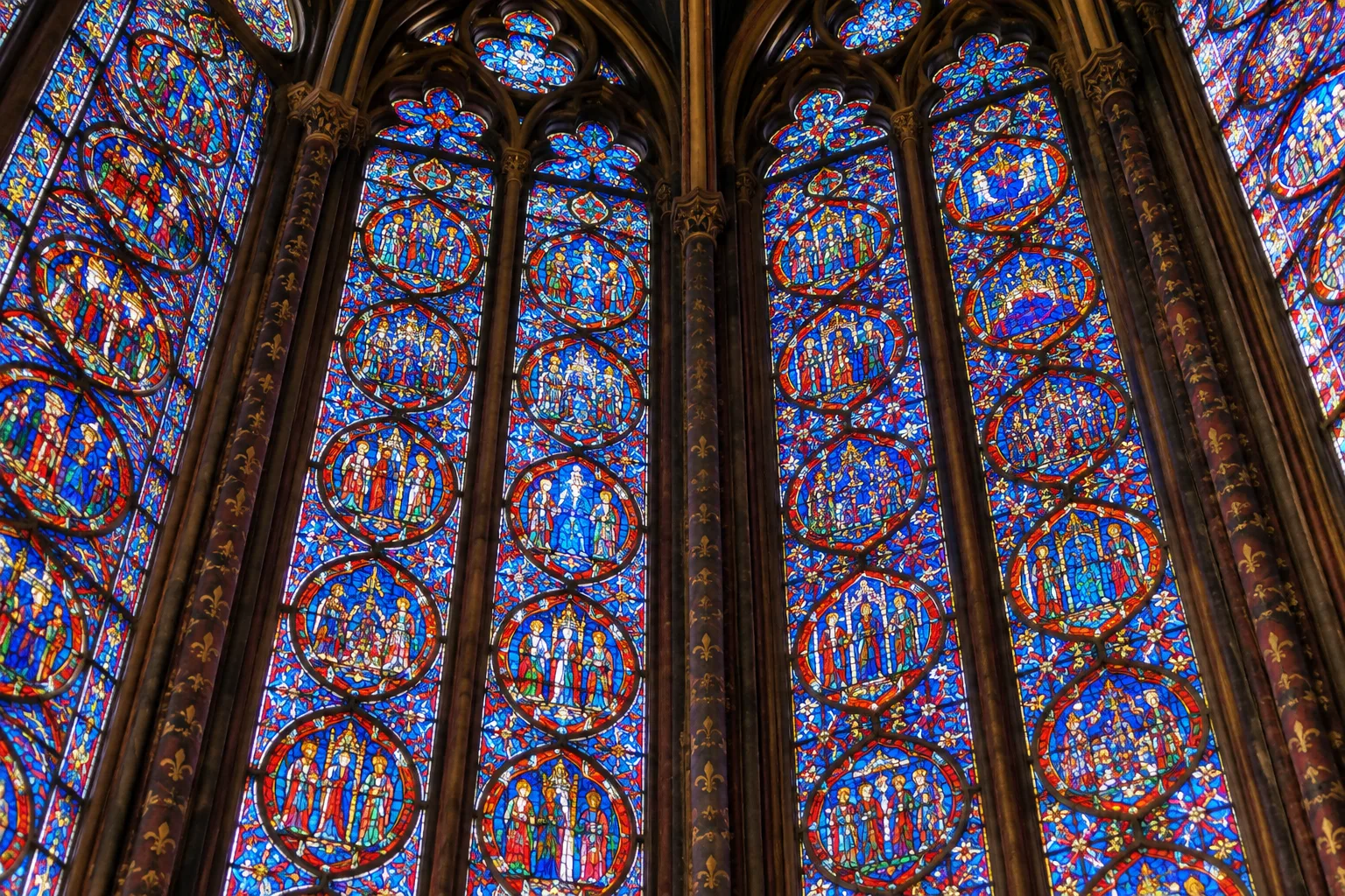 Détail des vitraux rouges et bleus de la chapelle supérieure, divisés par de fins meneaux de pierre.