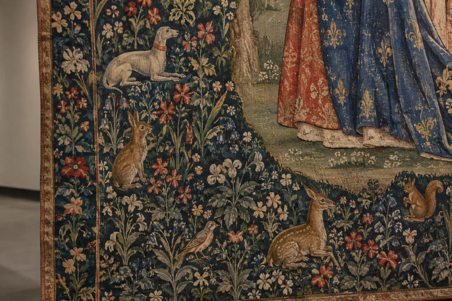 Fleurs et petits animaux tissés dans le décor dense d’une tapisserie médiévale.