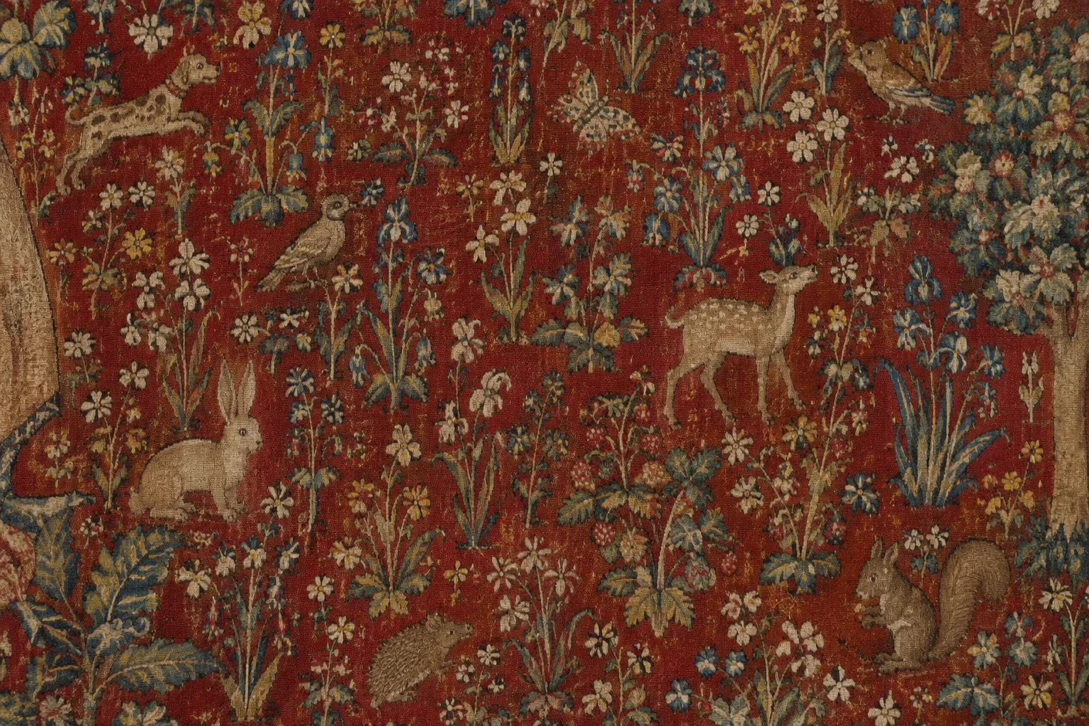 Détail d’une tapisserie médiévale où de petites fleurs et des animaux se détachent sur un fond rouge.