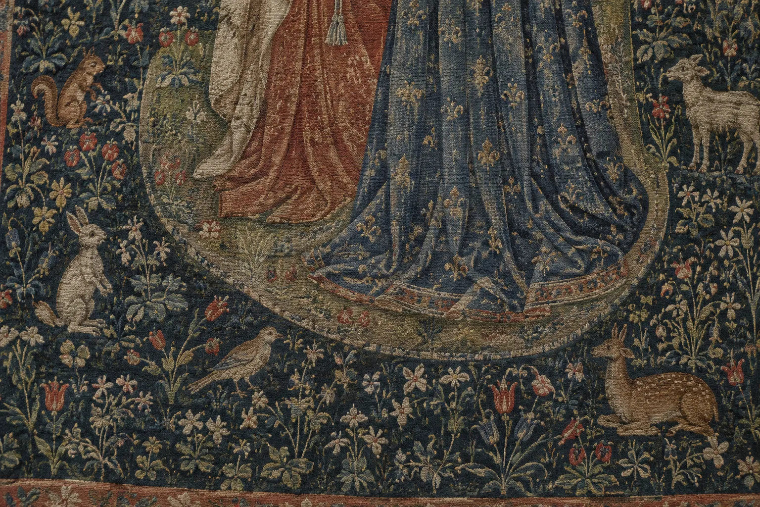 Détail d’une tapisserie médiévale où de petites plantes et des animaux apparaissent dans un tissage dense.