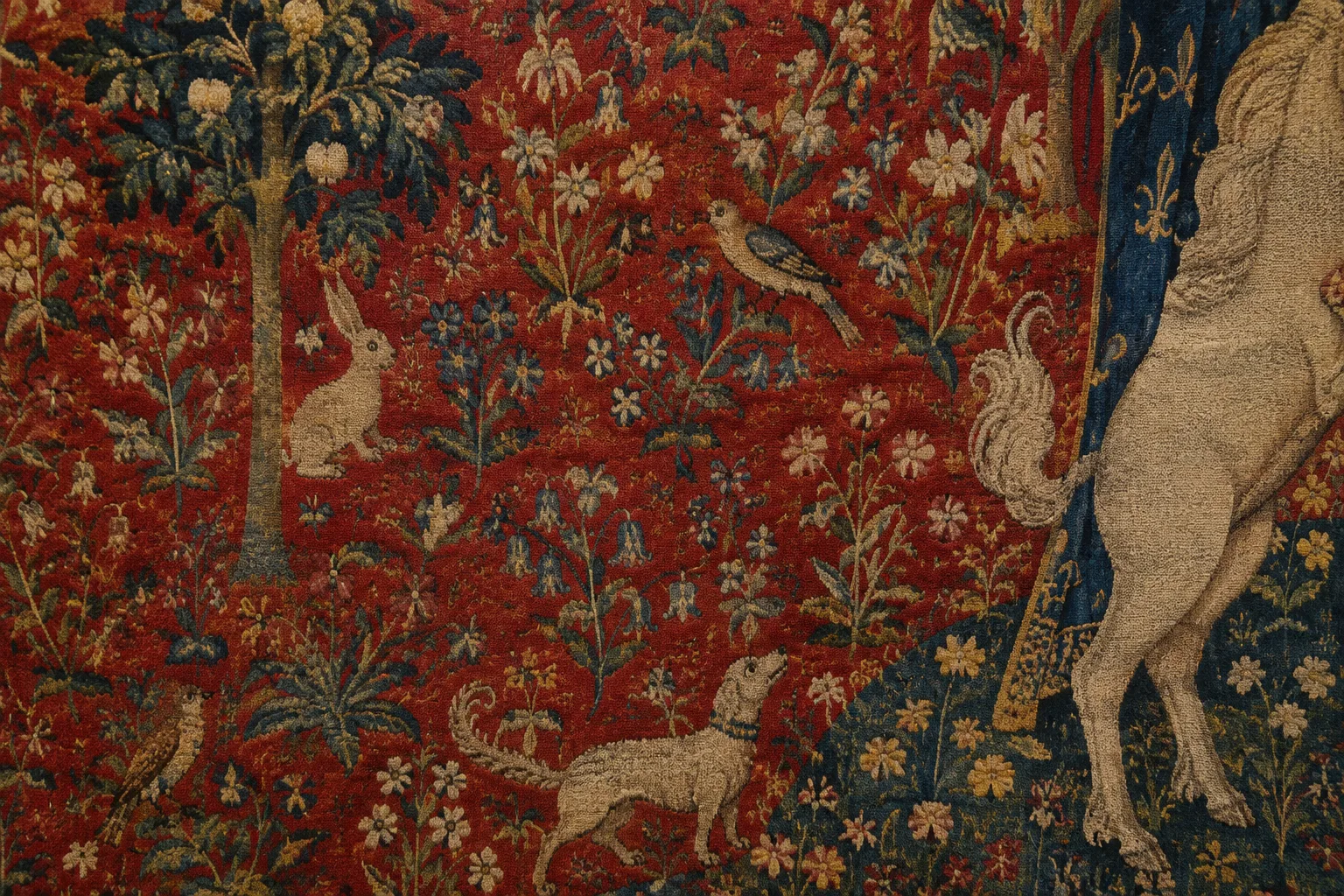 Détail d’une tapisserie médiévale où des fleurs et de petits animaux se détachent sur un fond rouge.