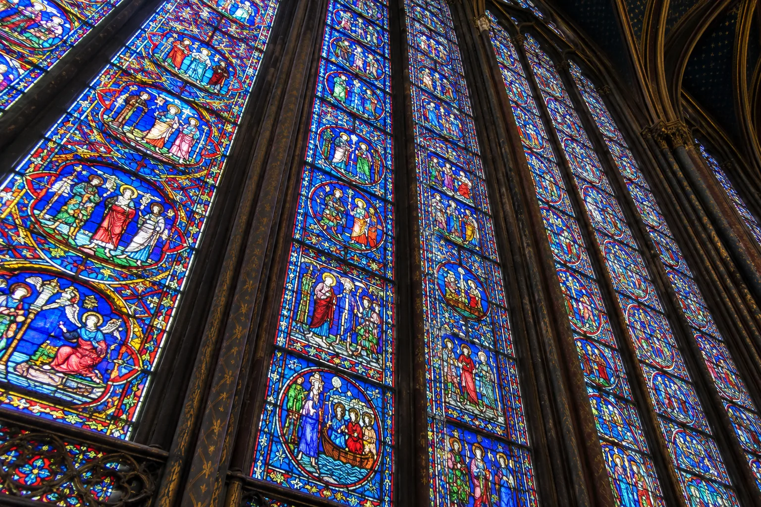 Détail en contre-plongée des panneaux colorés d’un vitrail médiéval, séparés par de fines pierres.